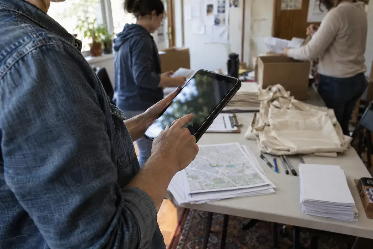 A volunteer coordinator using an iPad at a campaign check-in table with route maps and handouts.